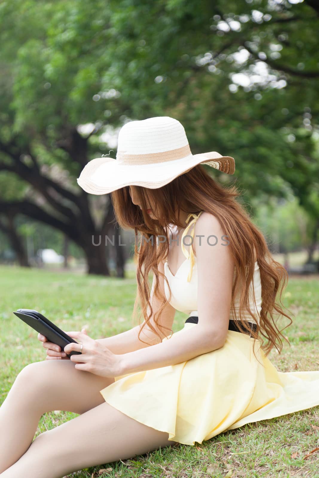 Woman sitting on grass and using a tablet. Located within the park.