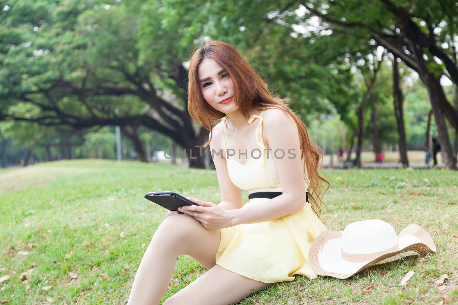 Woman sitting on grass and using a tablet. Located within the park.