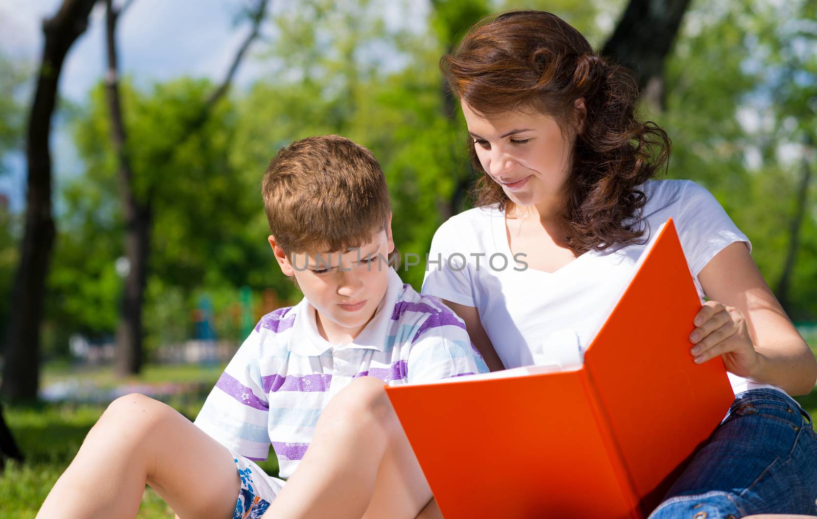 boy and a woman in a summer park reading a book together