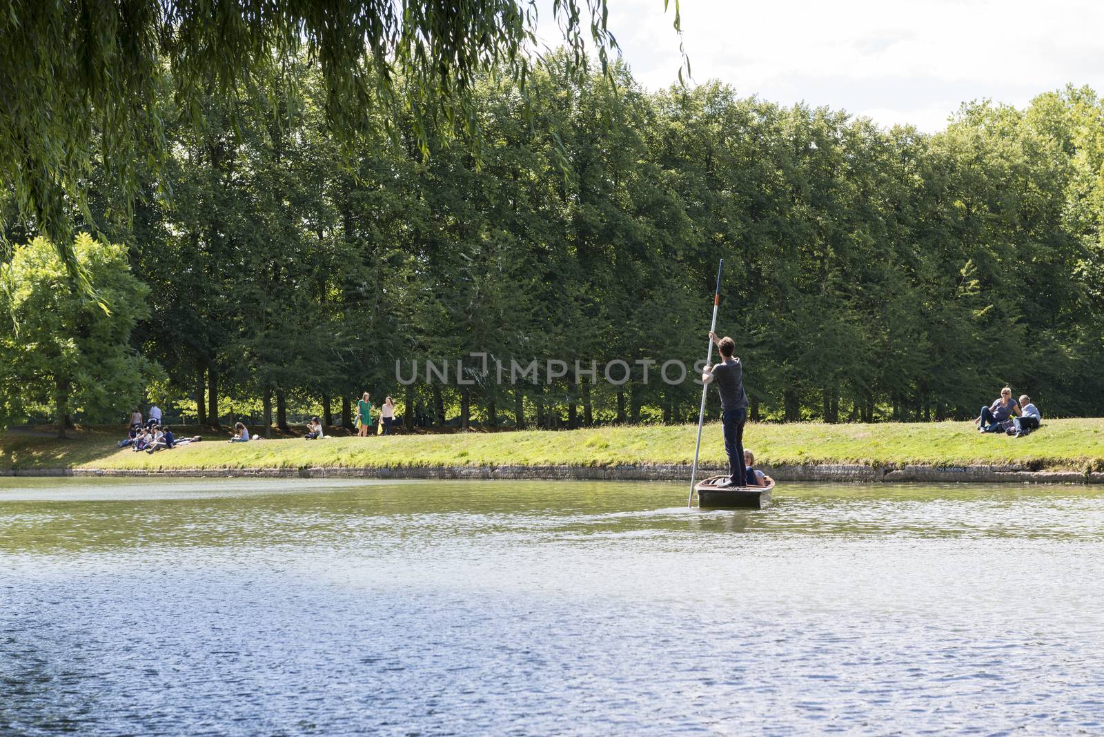 CAMBRIDGE, UK - AUGUST 18: Tourist punters in gondolas in River Cam with park full of trees in the background. August 18, 2013 in Cambridge.