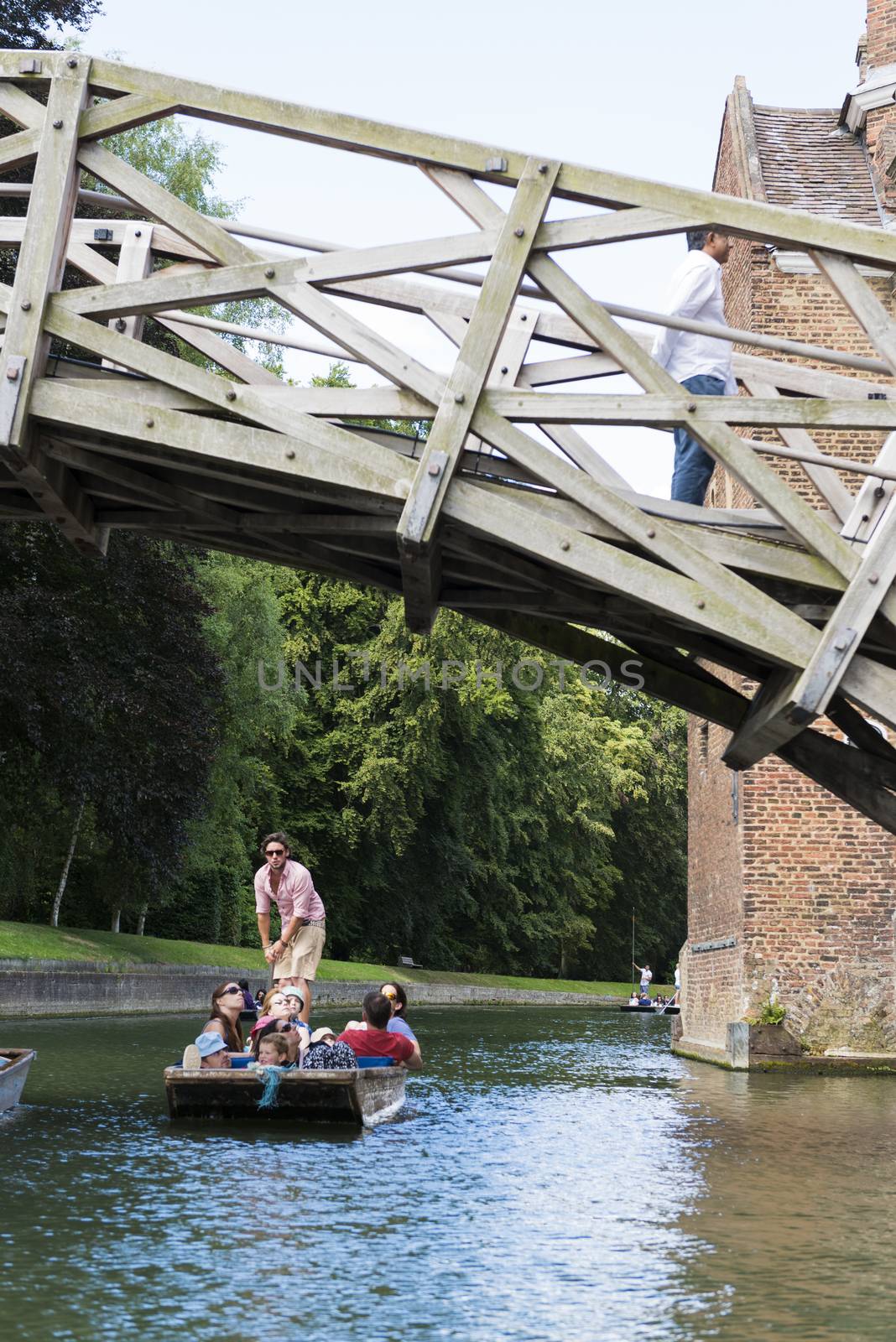 CAMBRIDGE, UK - AUGUST 18: Tourist punter in gondola in River Cam passing under Mathematical bridge with park full of trees in the background. August 18, 2013 in Cambridge.