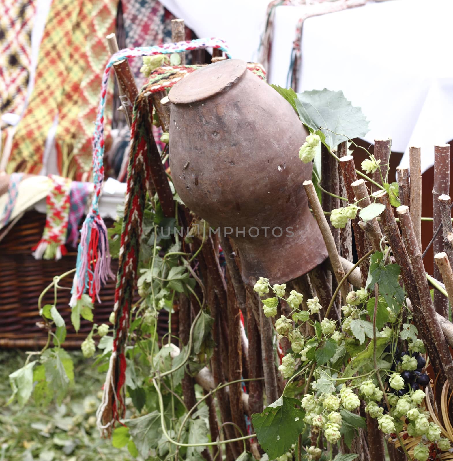 Clay pitcher hangs on wooden fence from woven tree branches