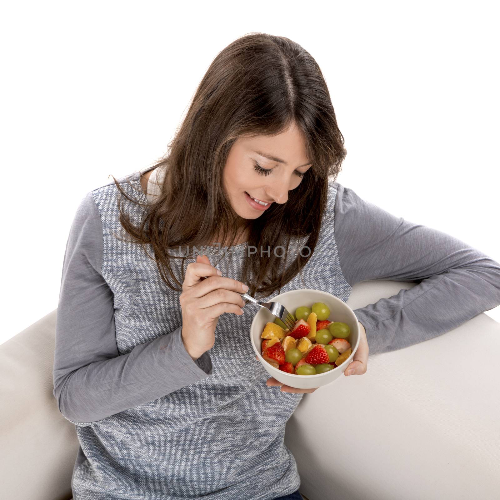 Beautiful woman relaxing on the sofa and eating a fruit salad