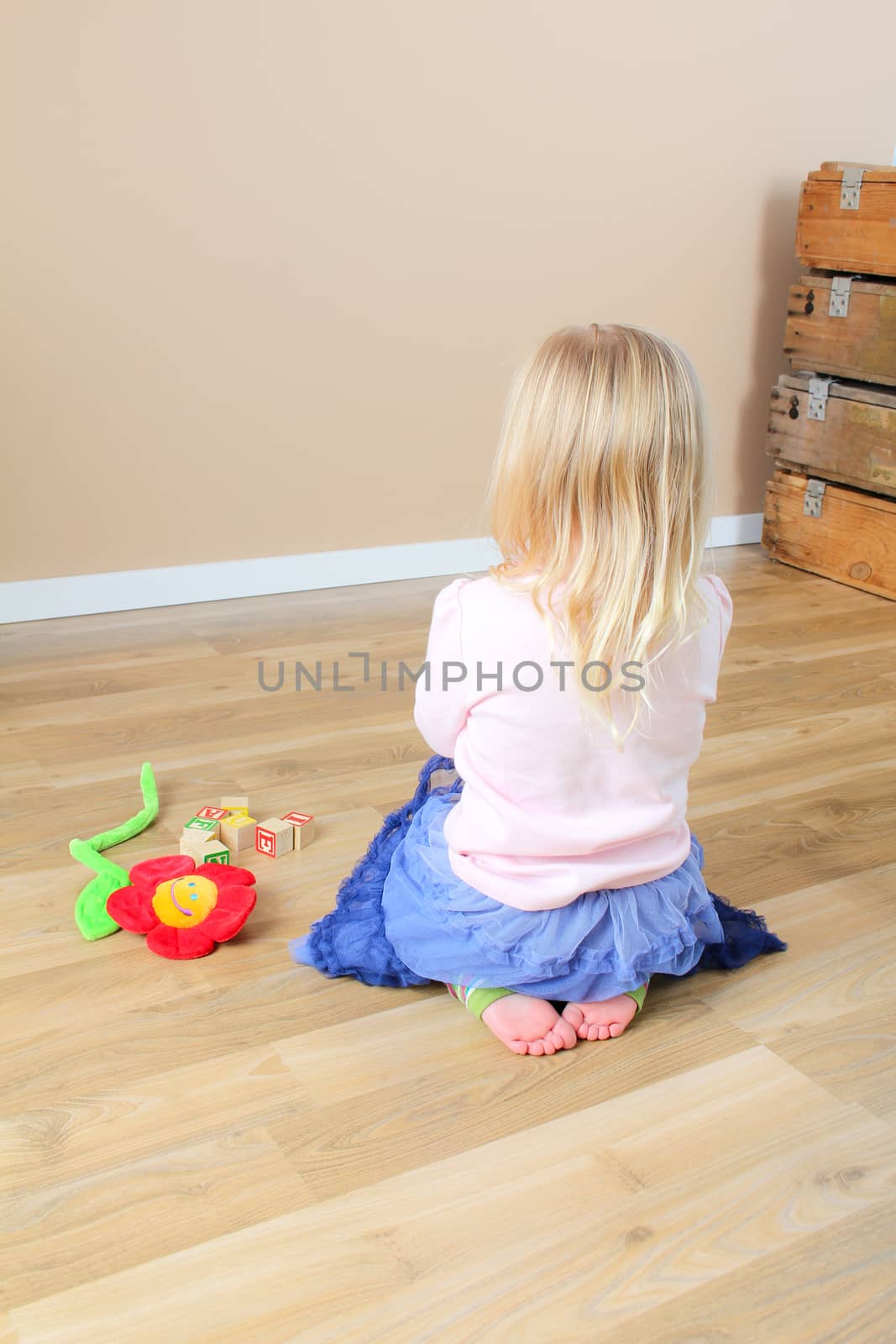 Little girl playing on a wooden floor wearing pink and blue
