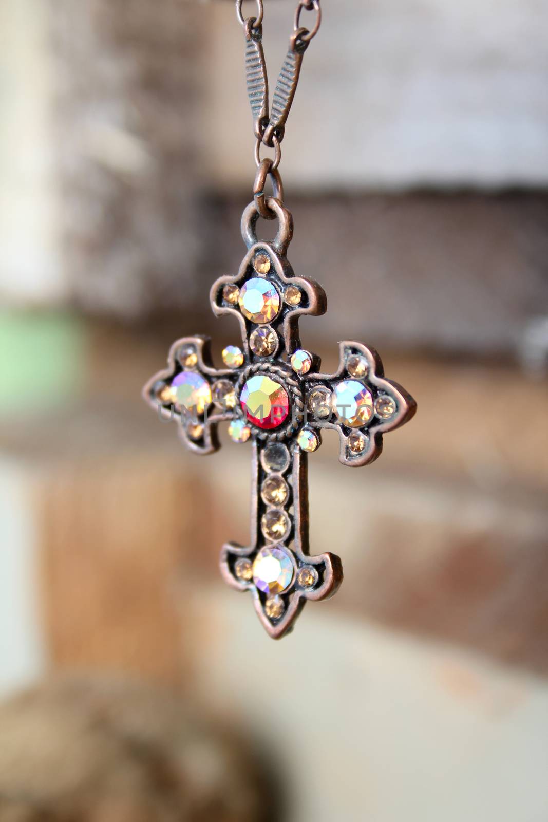 Gem filled copper cross on necklace against wooden background