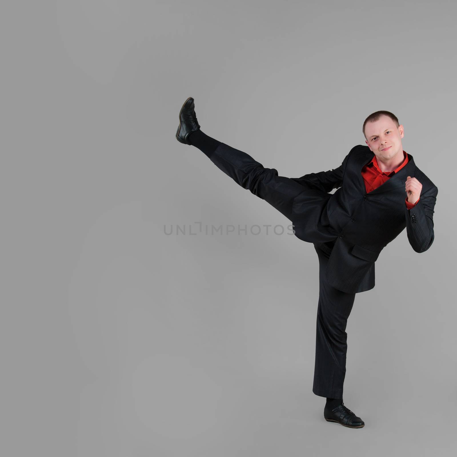 Businessman demonstrates a high kick on gray background