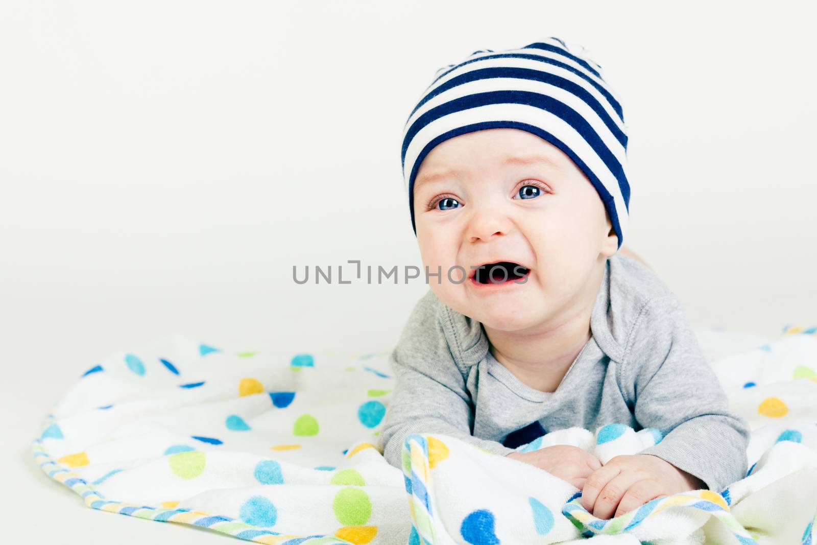 Portrait of a cute baby in striped hat lying down on a blanket