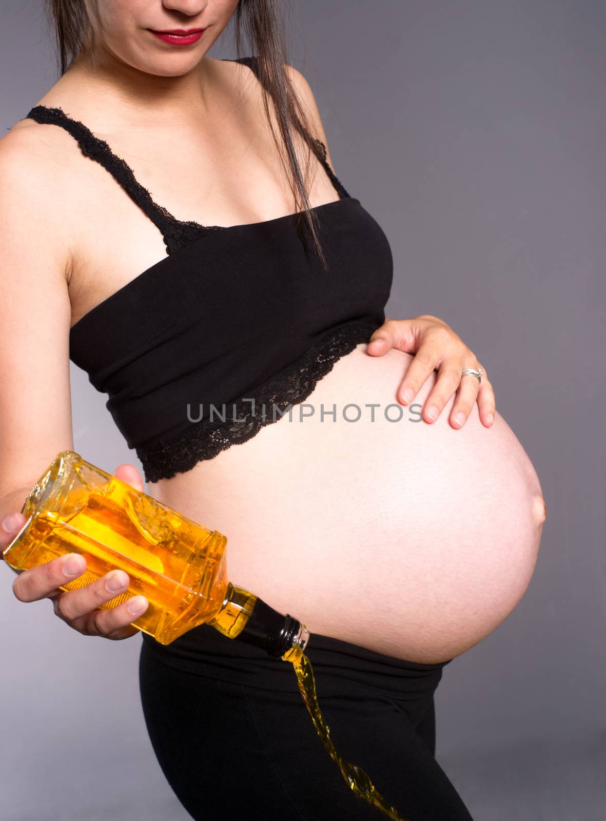 Vertical composition of woman pouring out a bottle of hard whiskey during pregnancy