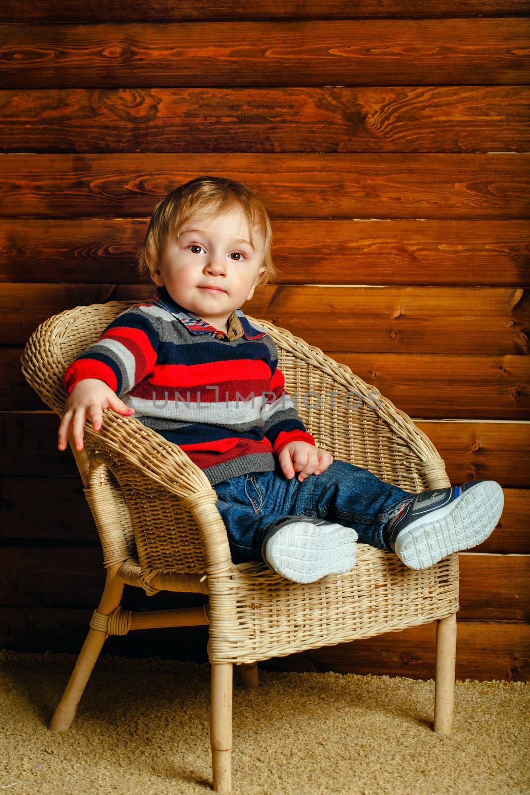 Little boy sitting in a wicker chair in a wooden house
