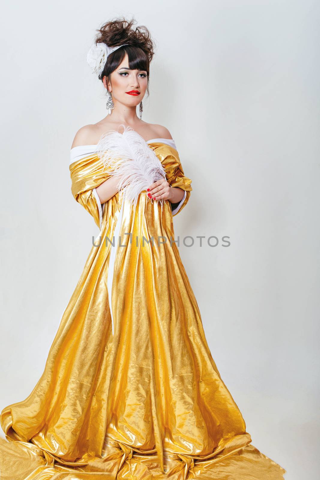 Young attractive girl in a long dress gold color holding a feather in her hands