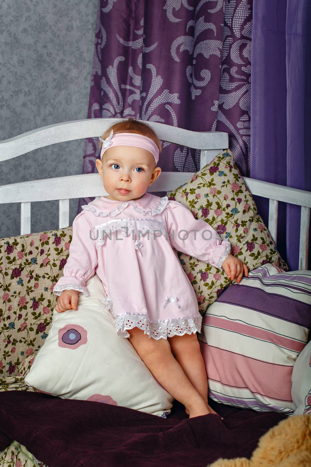 Little girl in the nursery stands leaning on pillows on a cot