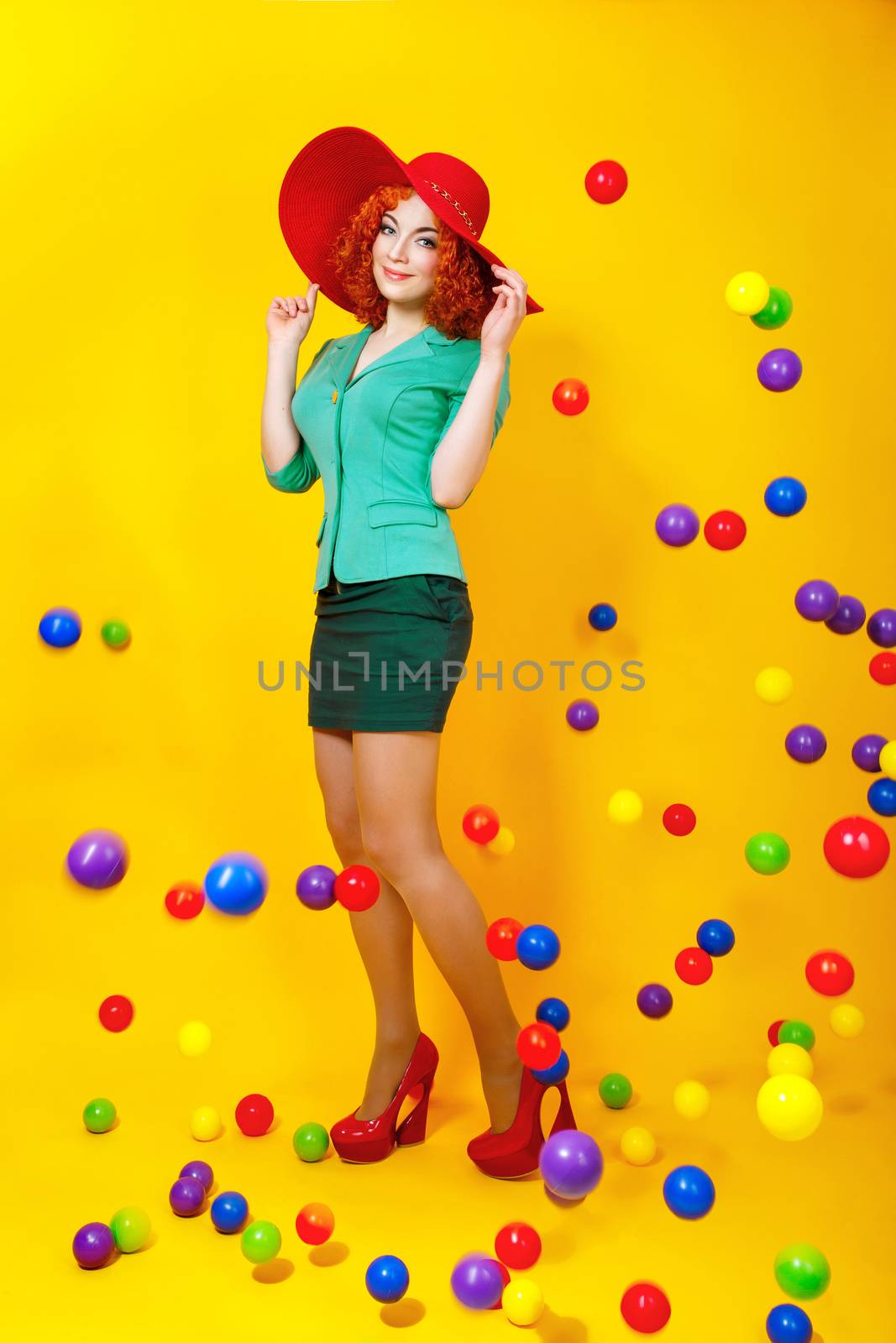 Young attractive girl in a hat on a yellow background, fall around the plastic balls