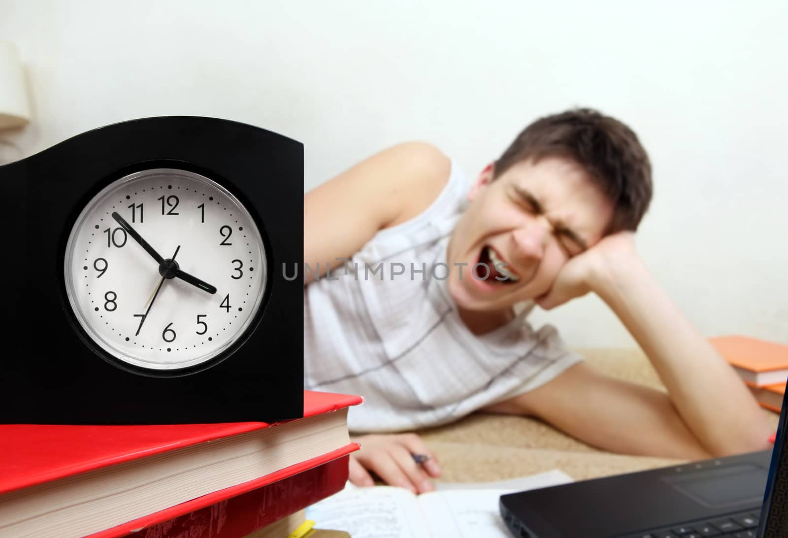 Tired Teenager doing Homework and Yawning at the Home. Focus on the Clock