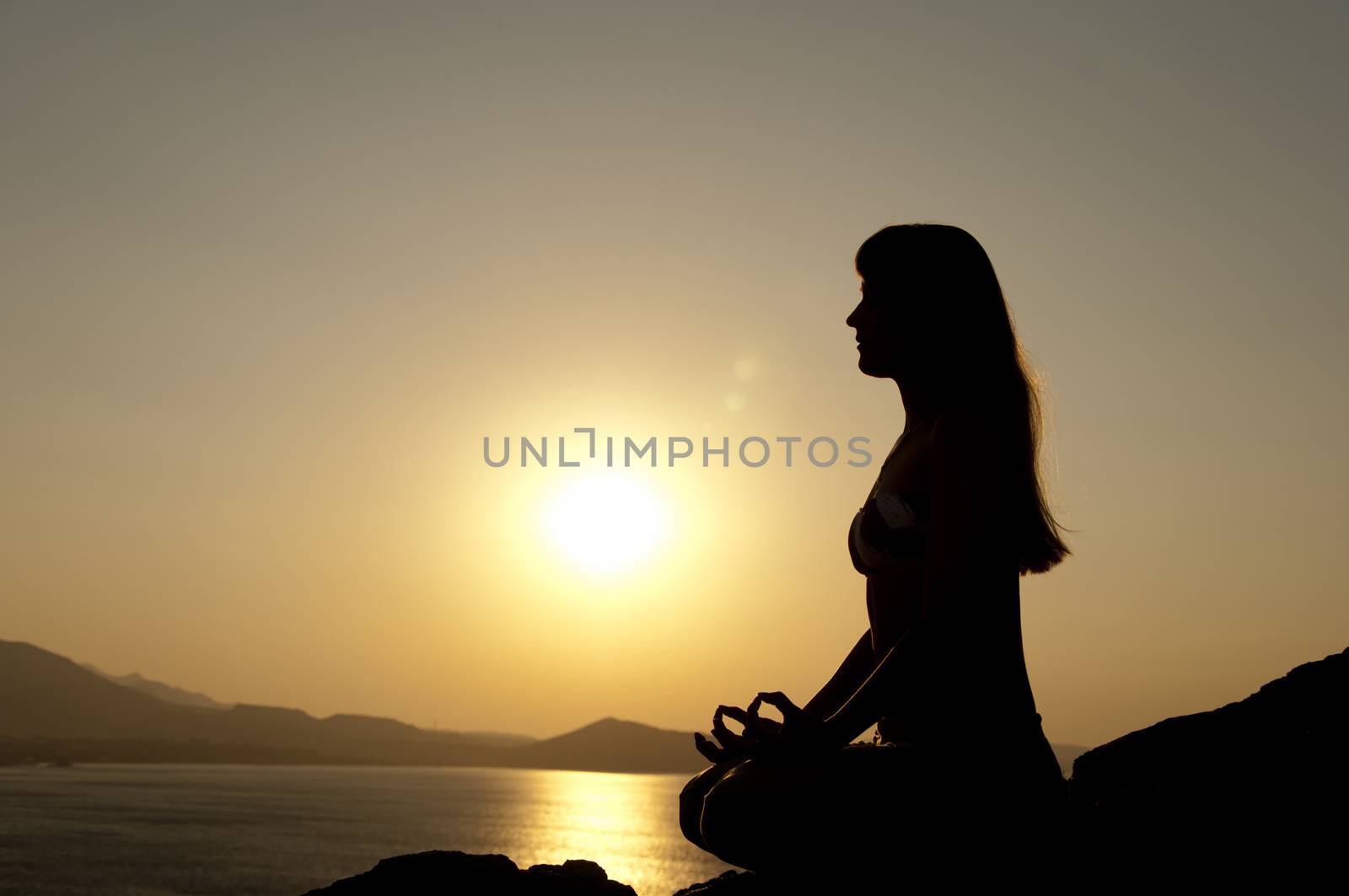Young model is doing yoga on seaside at sunrise