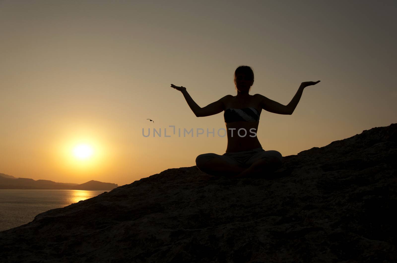 Young model is doing yoga on seaside at sunrise