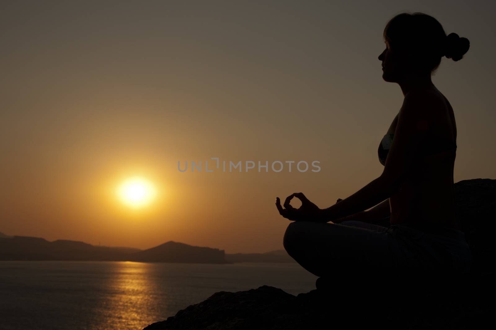 Young model is doing yoga on seaside at sunrise