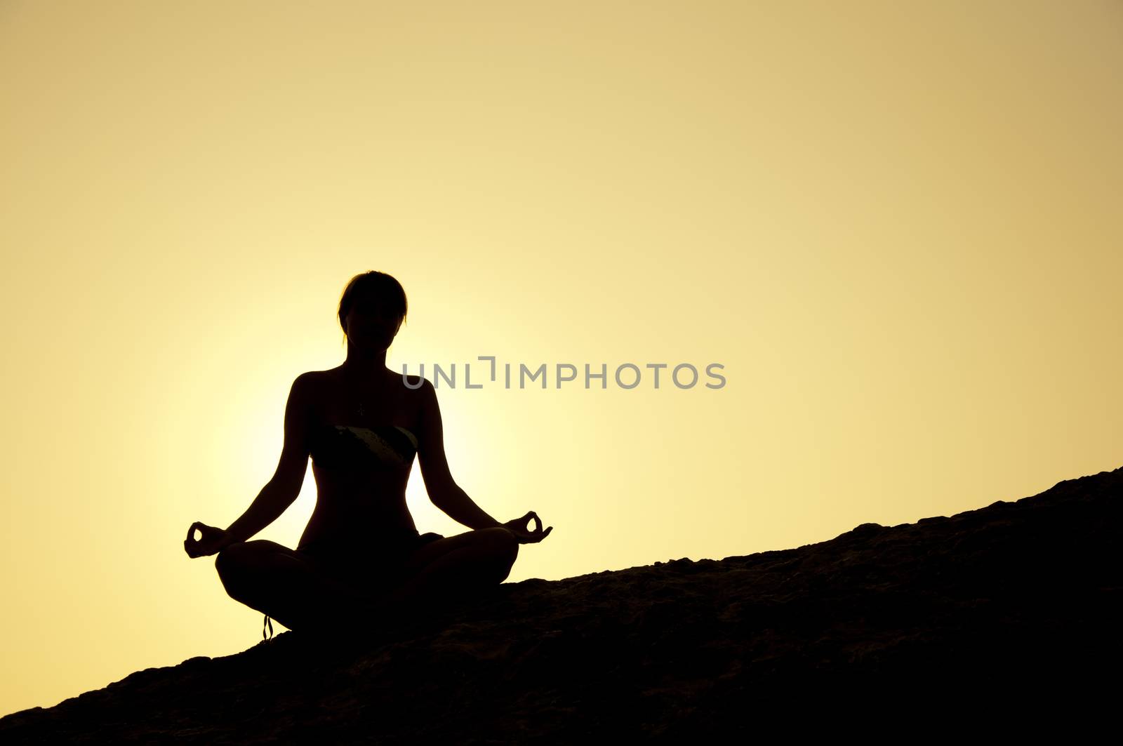 Young model is doing yoga on seaside at sunrise