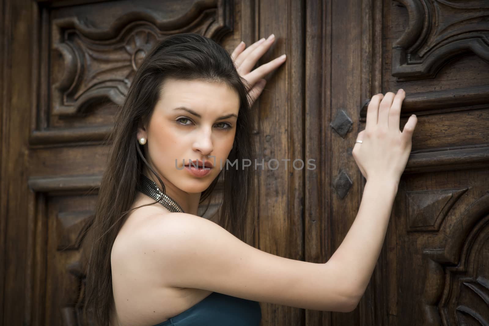 Pretty brunette girl outdoors with elegant dress leaning against old wood doors