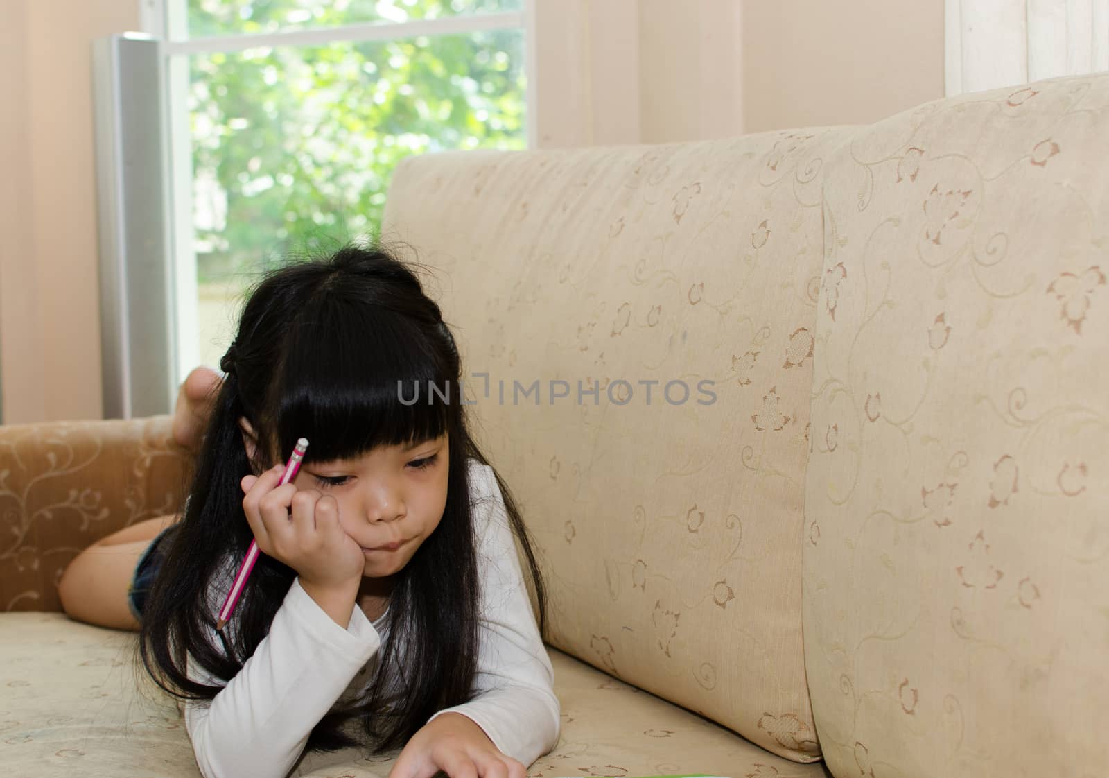 Cute little girl writing on a sofa.