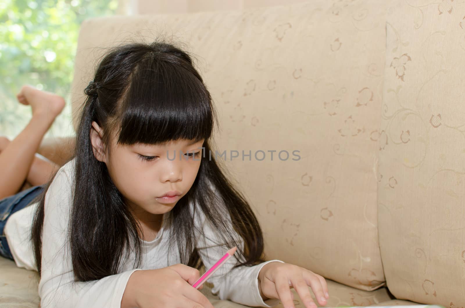 Cute little girl writing on a sofa.