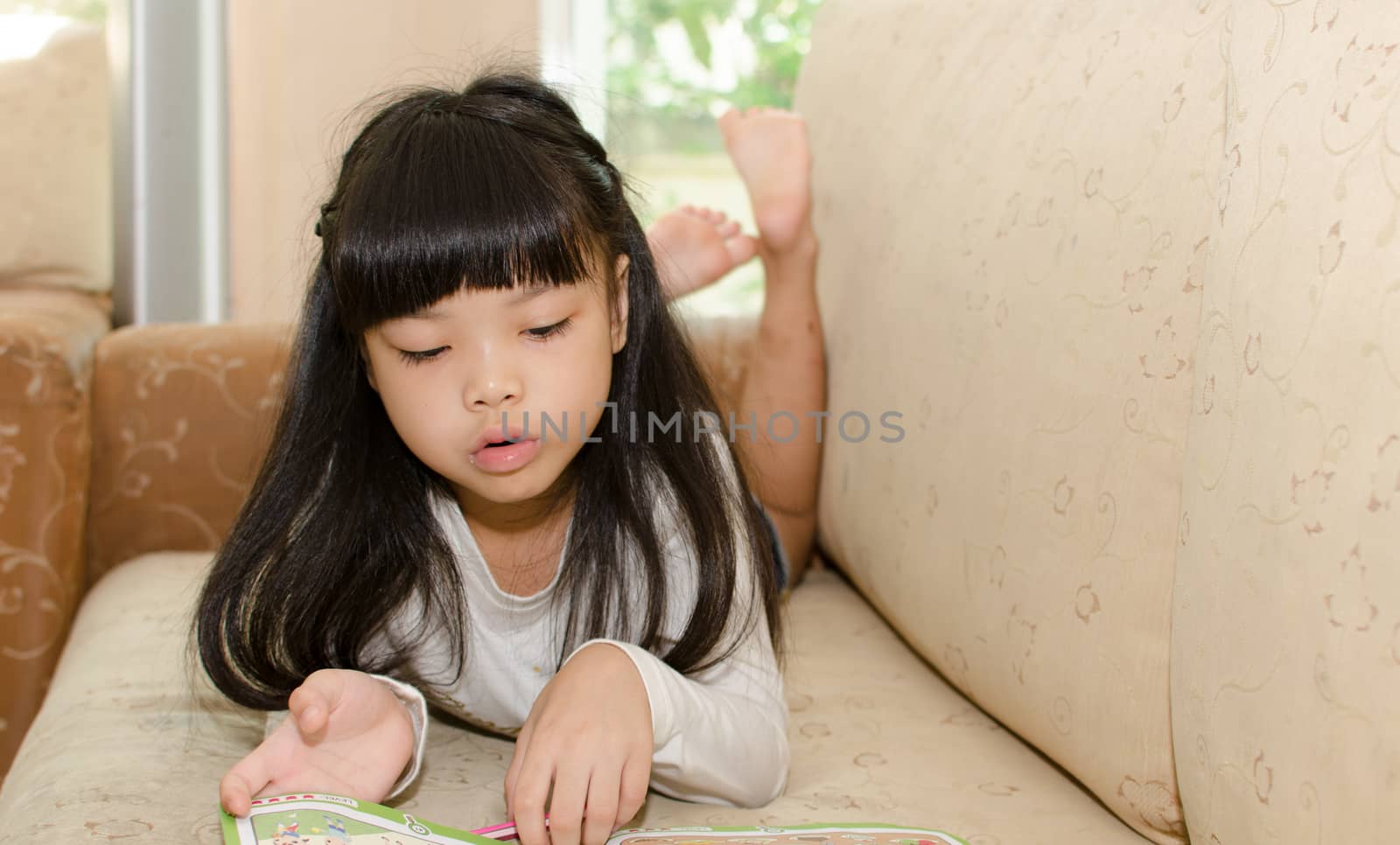 Cute little girl writing on a sofa.