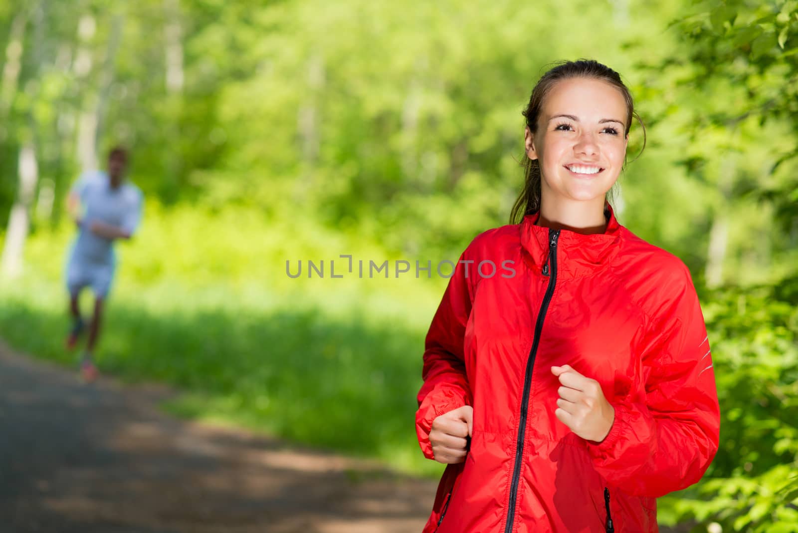 healthy young female athlete running in a summer park smiling and happy while working out
