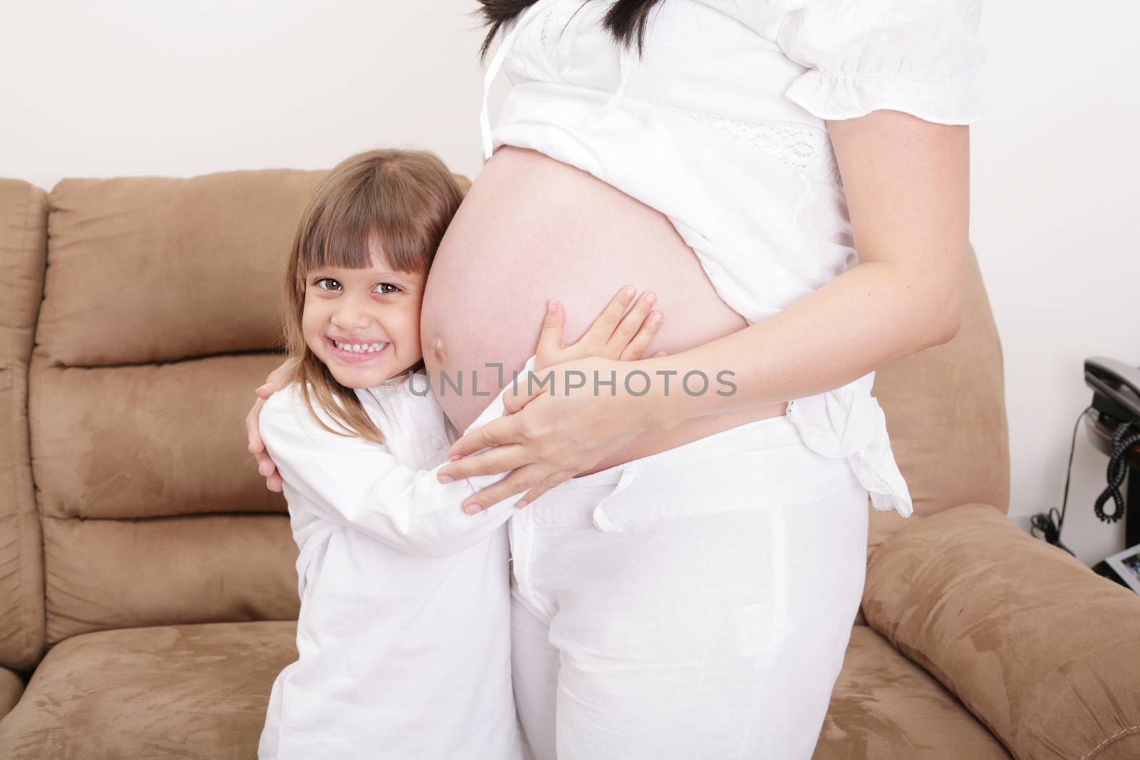 Smiling girl listening to the abdomen of her mother.