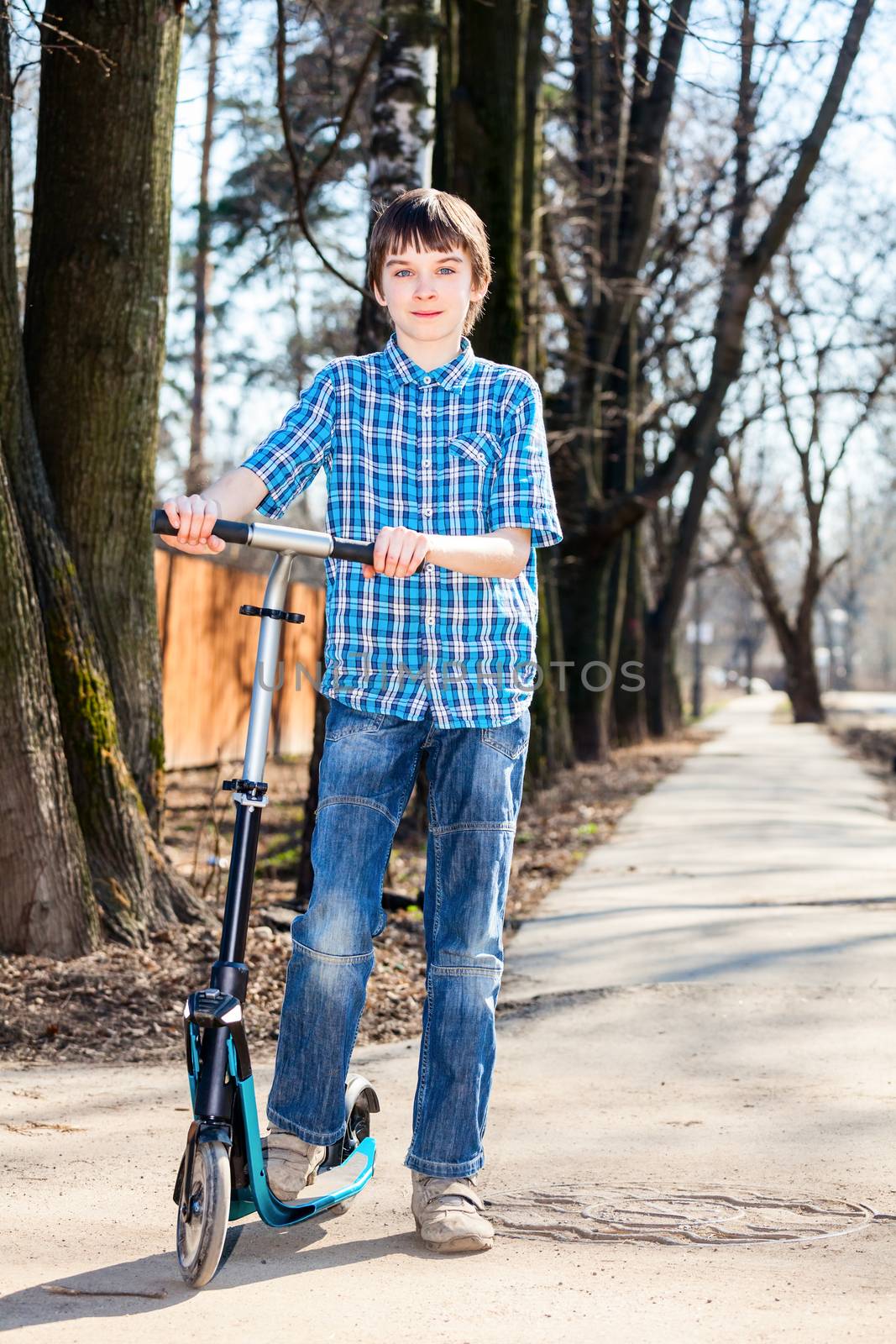 Cute boy standing with his push scooter outdoors