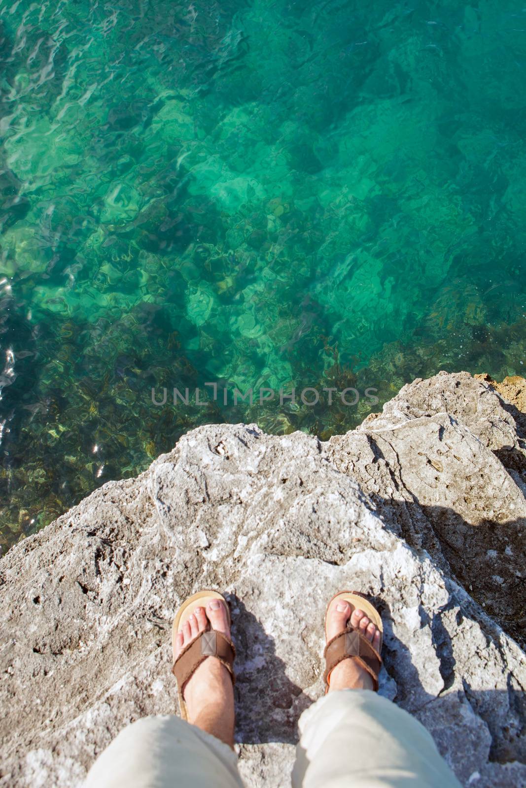 Self portrait showing a mans feet standing on the edge of a cliff by the tropical ocean waters in Bermuda.
