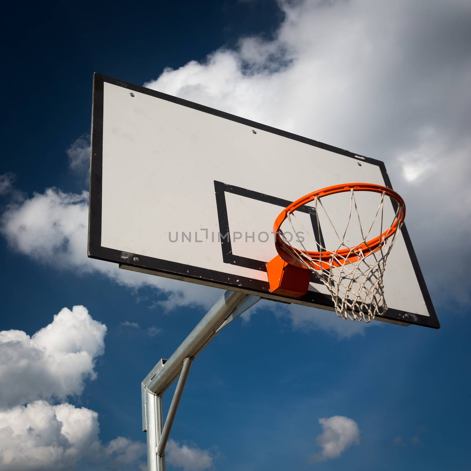 Basketball hoop against  lovely blue summer sky with some fluffy white clouds