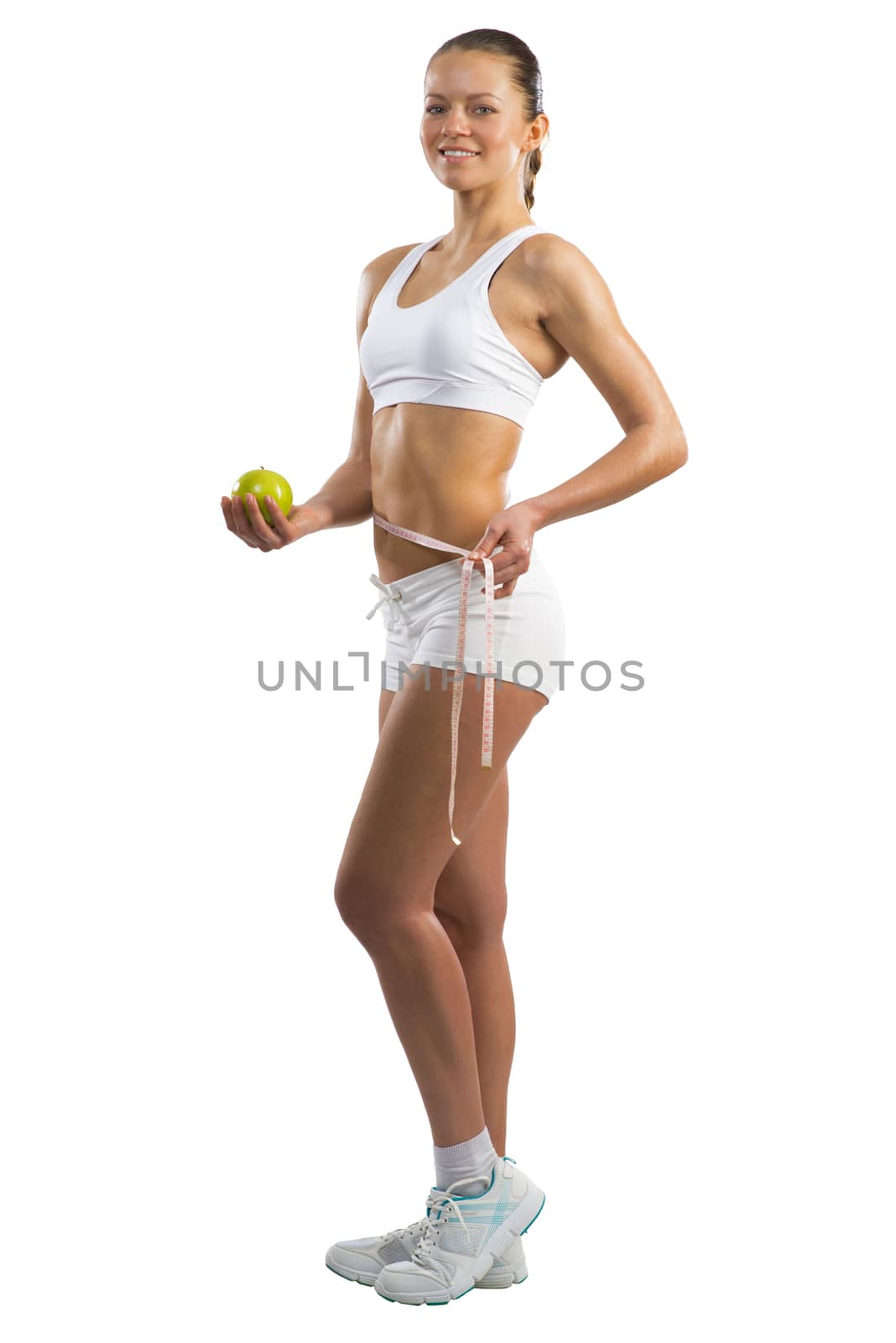 young athletic girl measuring waist measuring tape and holding a green apple, concept of healthy eating, isolated on white background