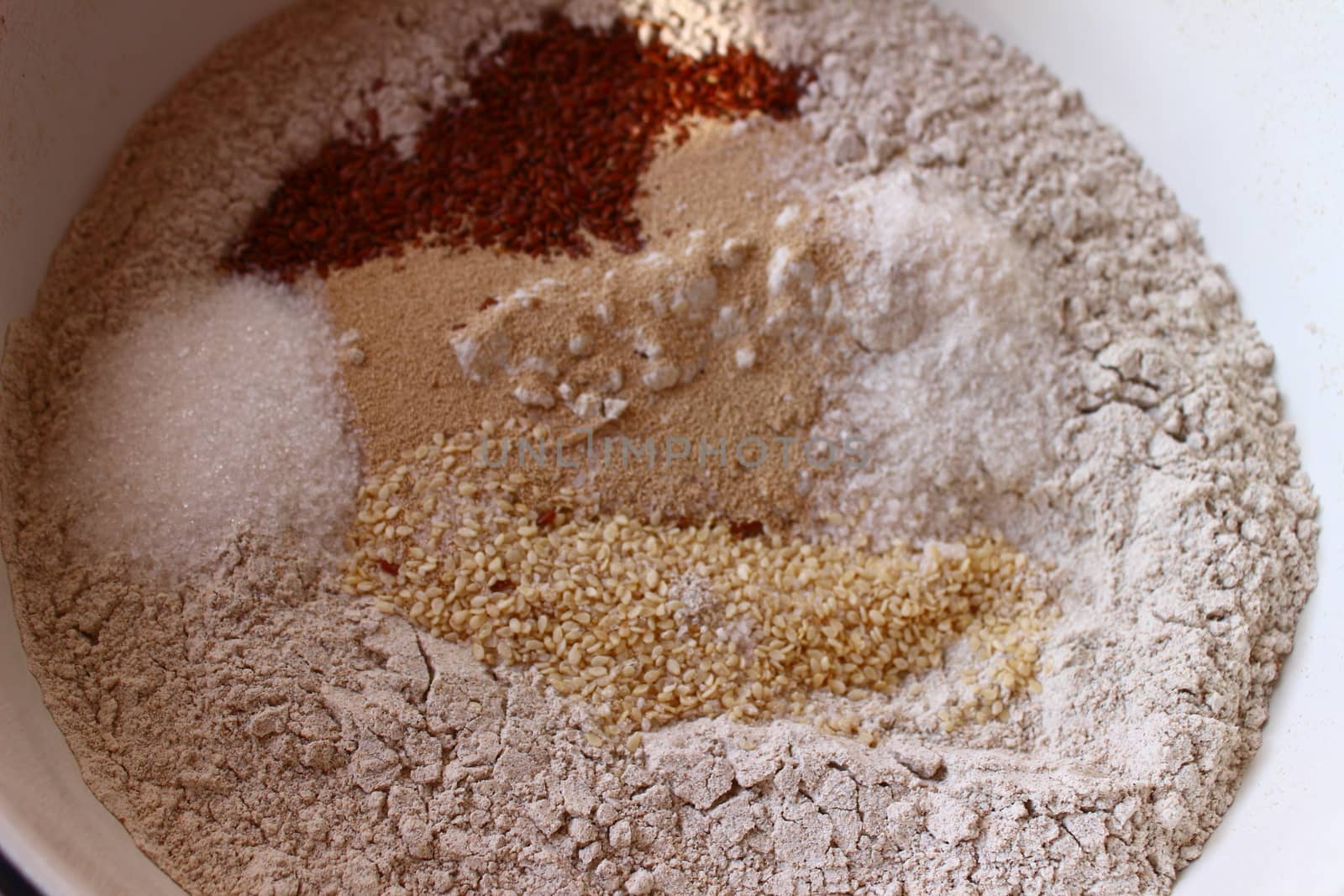 in a white bowl blank for making bread: flour, salt, sugar, yeast, flax seeds, sesame seeds