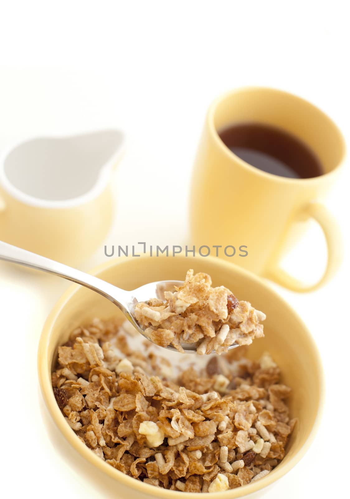 Eating a bowl of healthy muesli for breakfast with a mouthful raised on a spoon and a mug of coffee in the background