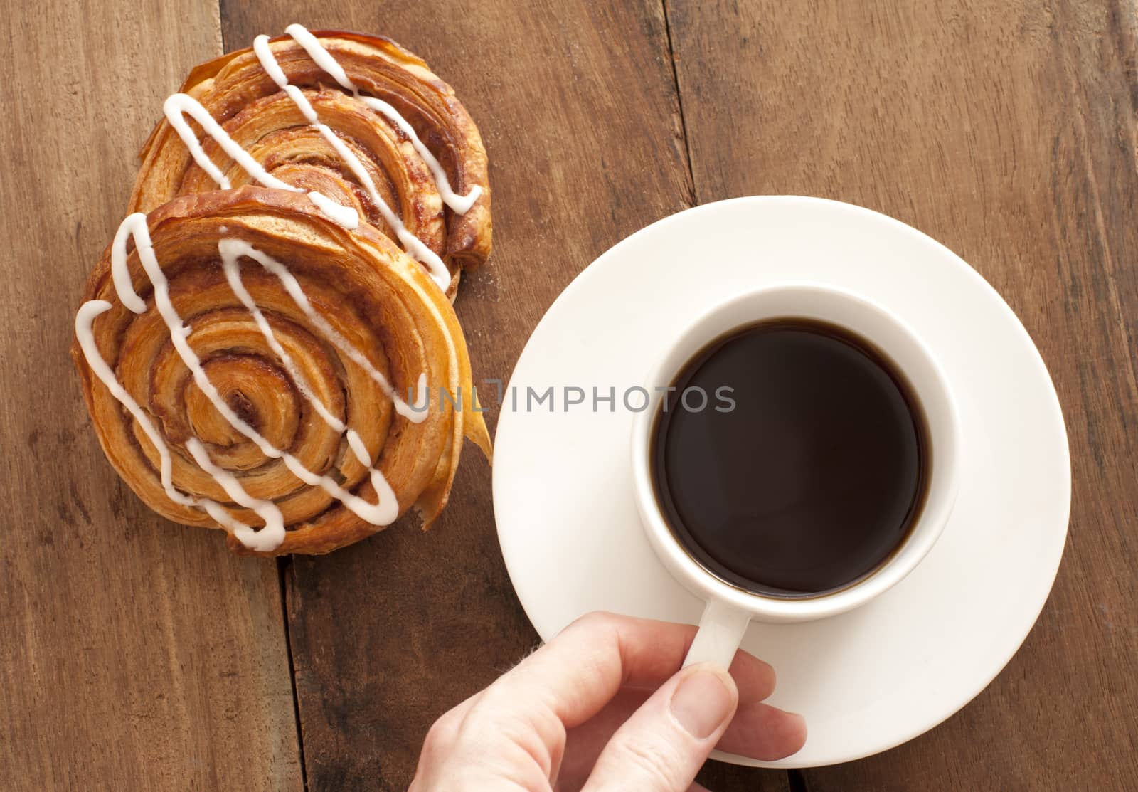 Man reaching for a cup and saucer of full roast espresso coffee with fresh Danish pastries for a refreshing coffee break, high angle view on wood