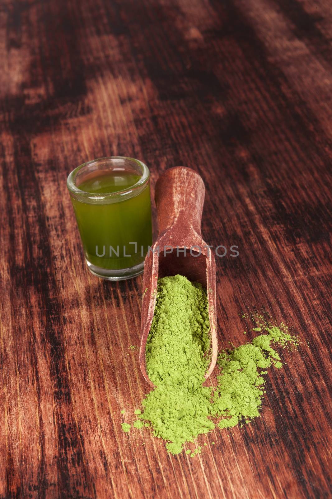 Green food supplement. Wheatgrass ground on brown wooden scoop on brown wooden background. Healthy natural detox. 