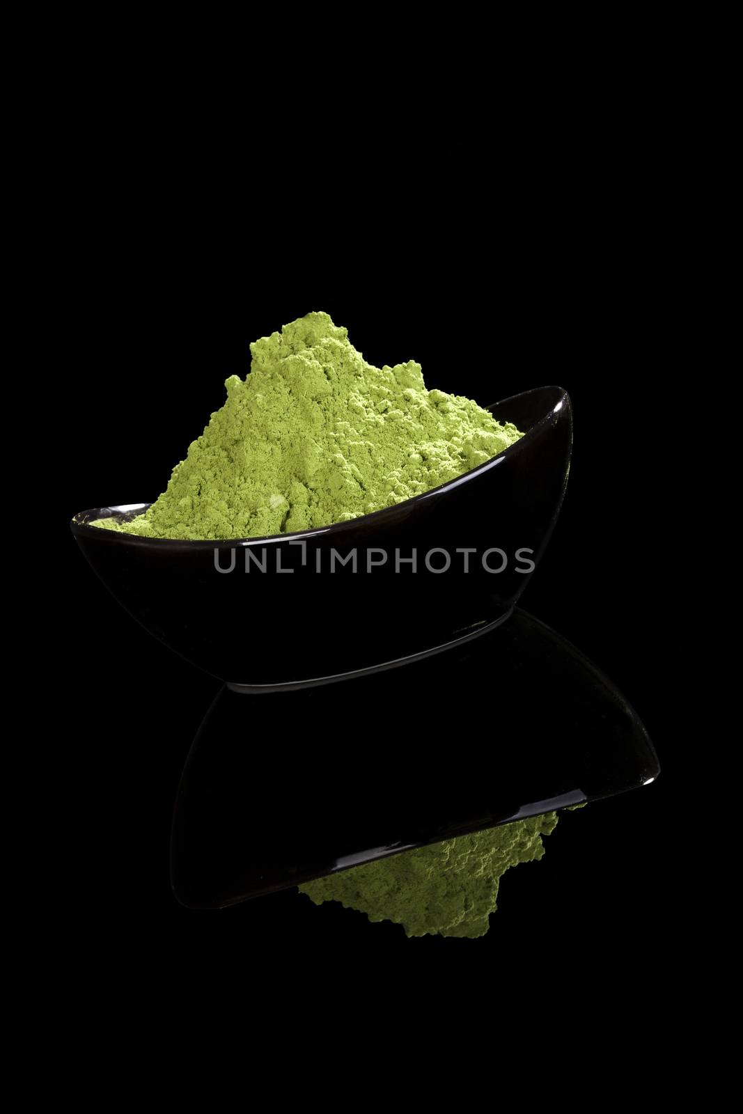 Green nutritional food supplement. Green ground wheatgrass powder isolated on black background.