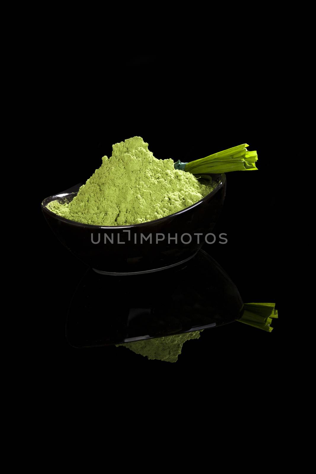 Green powder in bowl and grass blades isolated on black background. Healthy nutritional supplements. Green superfood, detox concept. 