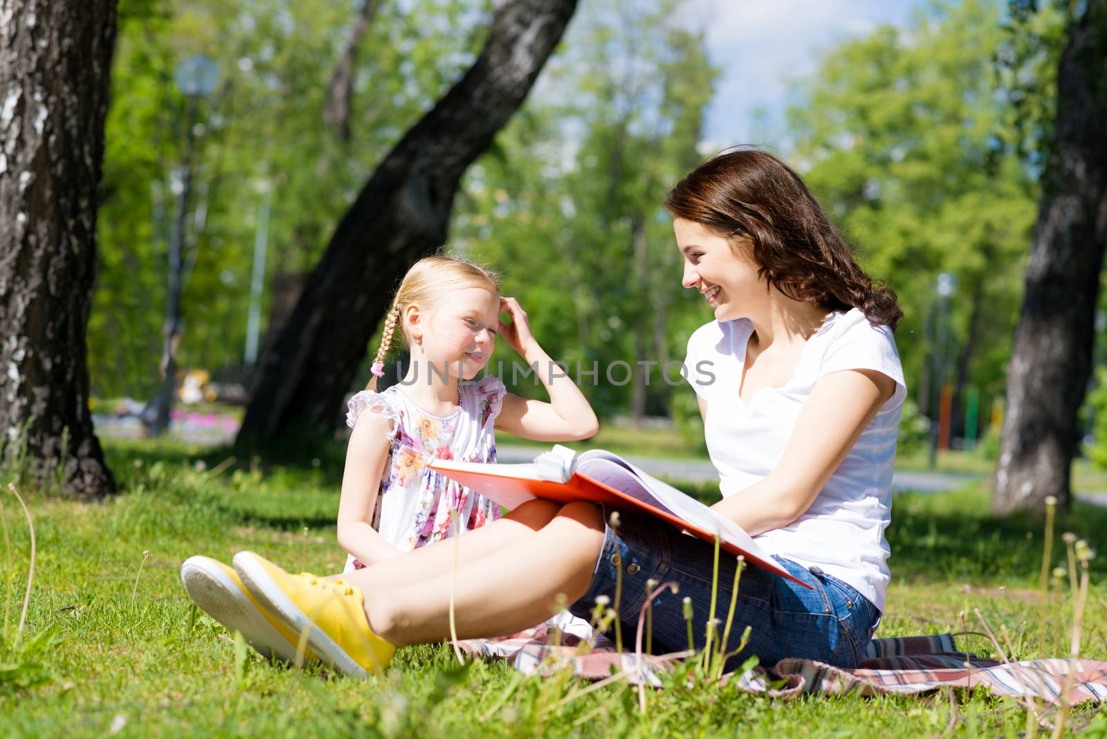 girl with the teacher reading a book together in the summer park