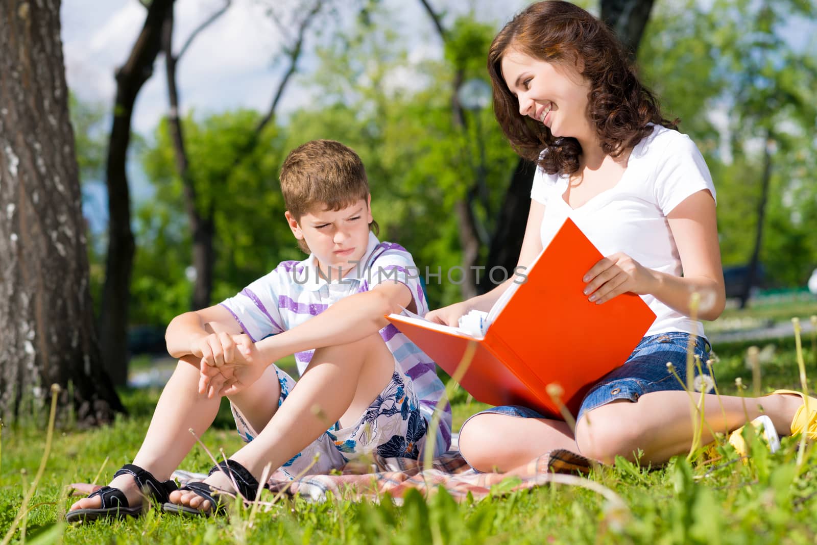 boy and a woman in a summer park reading a book together