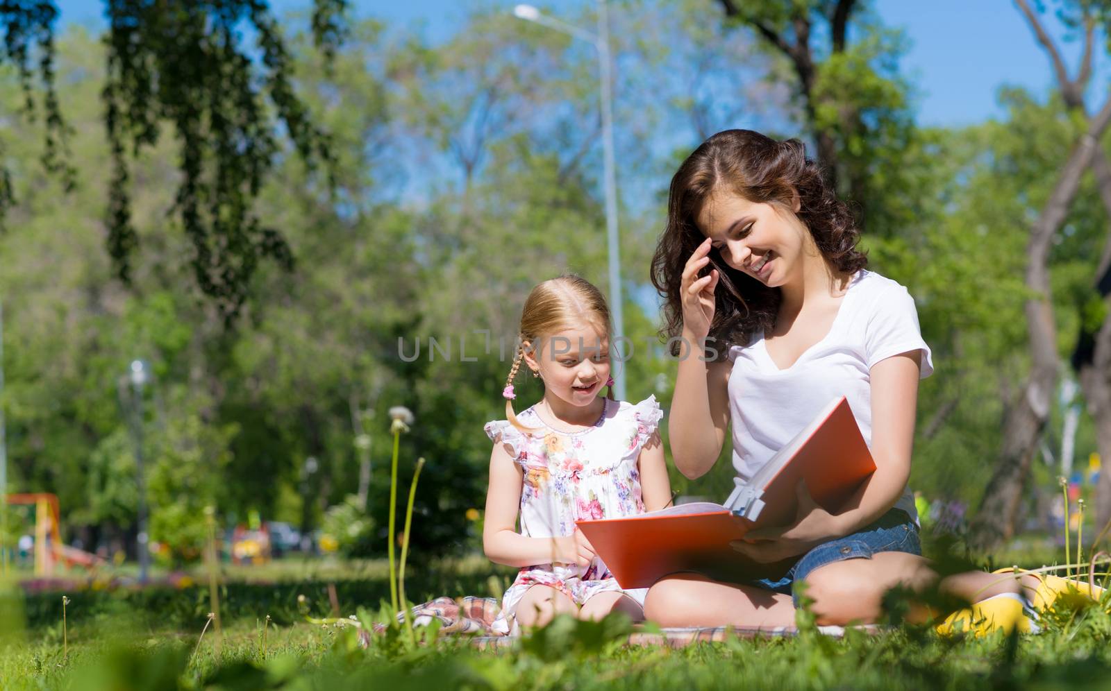 girl with the teacher reading a book together in the summer park