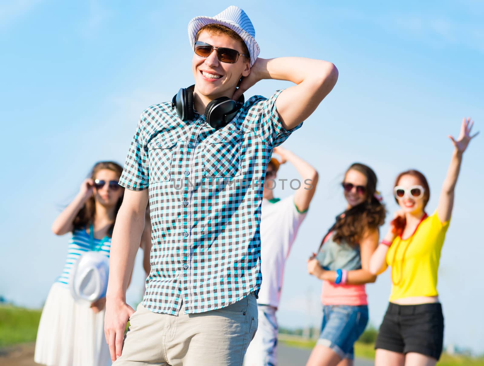 young man in sunglasses, a hat holds a hand on a background of blue sky and friends