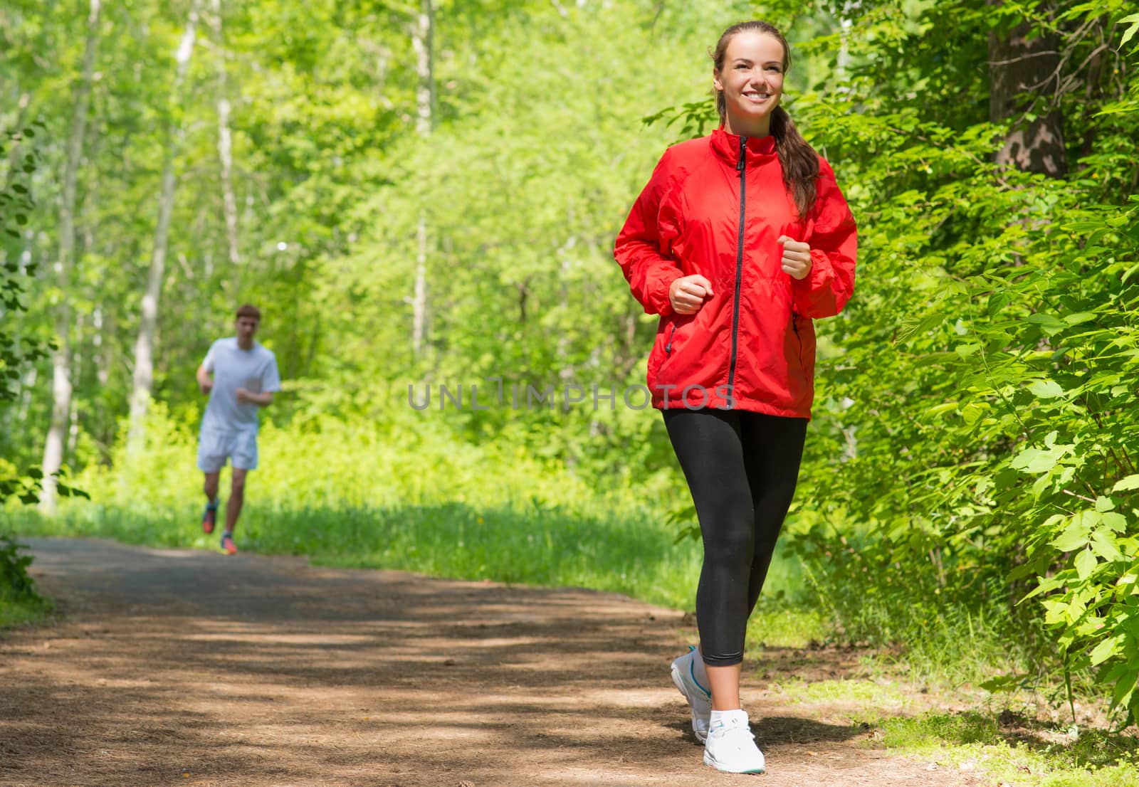 healthy young female athlete running in a summer park smiling and happy while working out