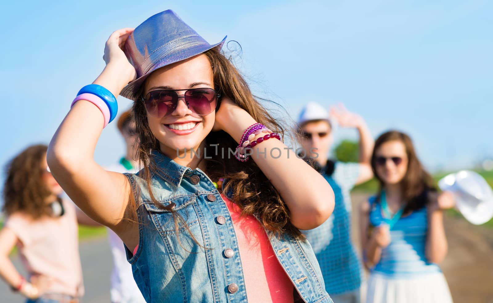 stylish young woman in sunglasses on the background of blue sky and friends