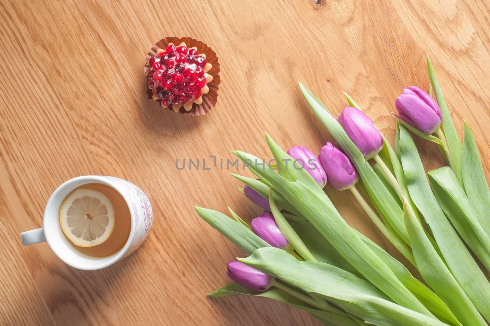 Fresh violet tulips, cake and tea on the wooden table