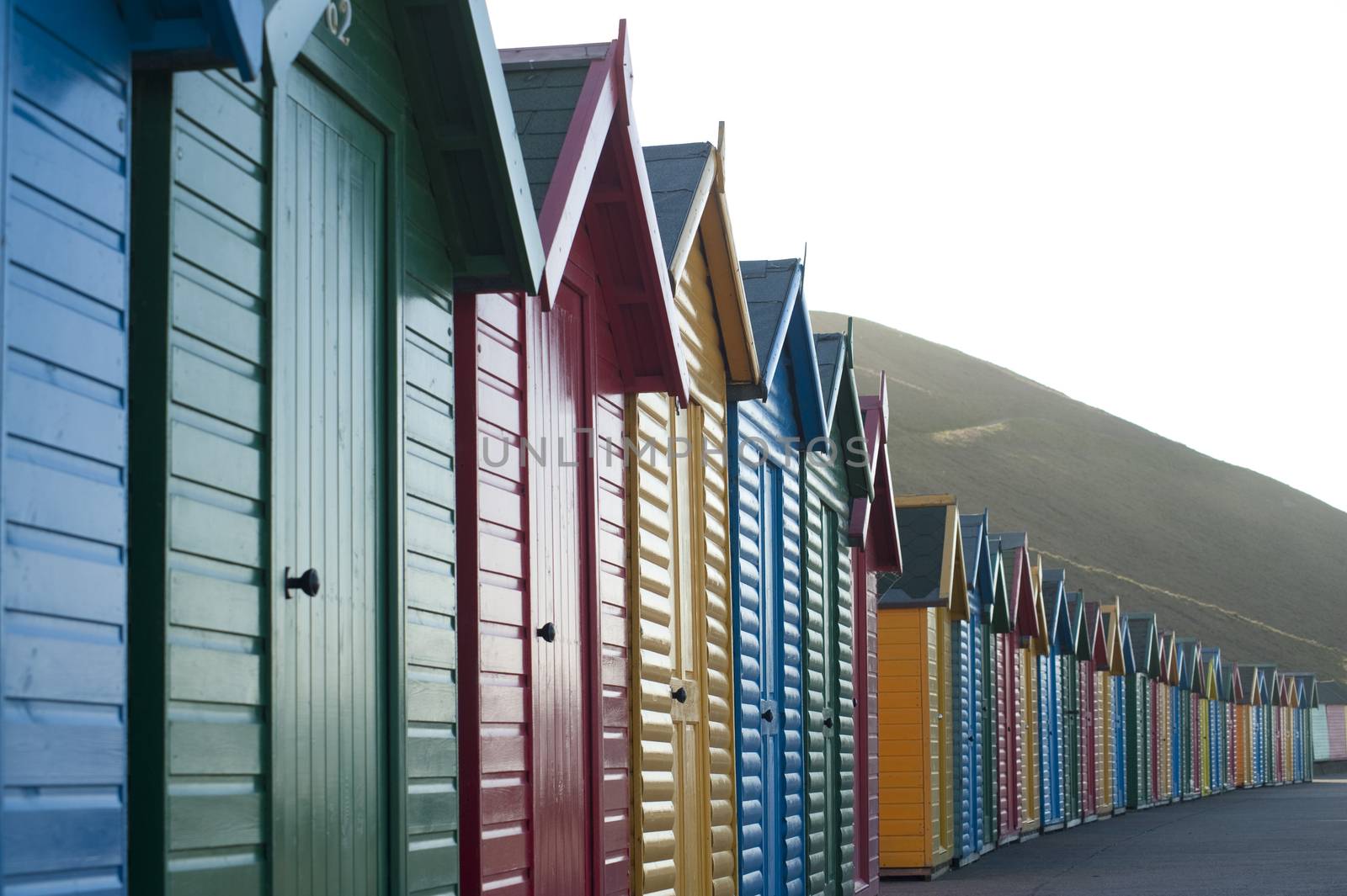 Row of colorful wooden beach huts overlooking Whitby Sands in North Yorkshire looking along the front facades of the receding line of huts