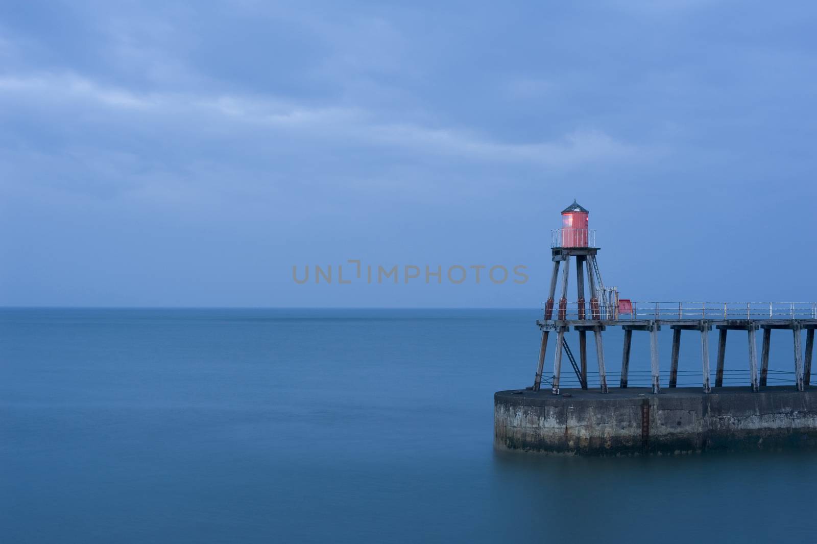 Whitby pier with one of the navigation beacons to guide shipping into the harbour at night on a calm ocean with copyspace
