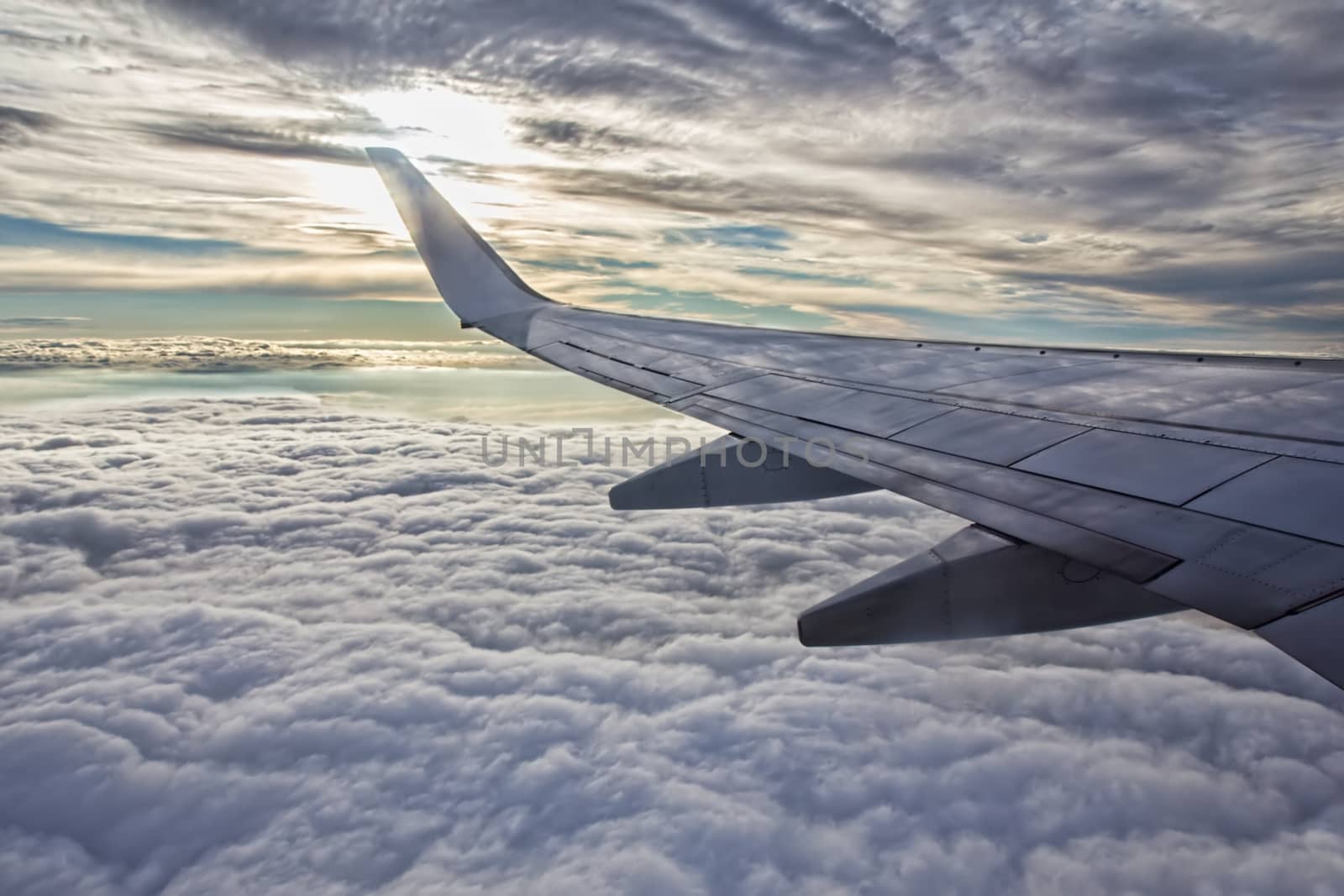 Sunset, cloudy sky and airplane wing as seen through window of an aircraft.