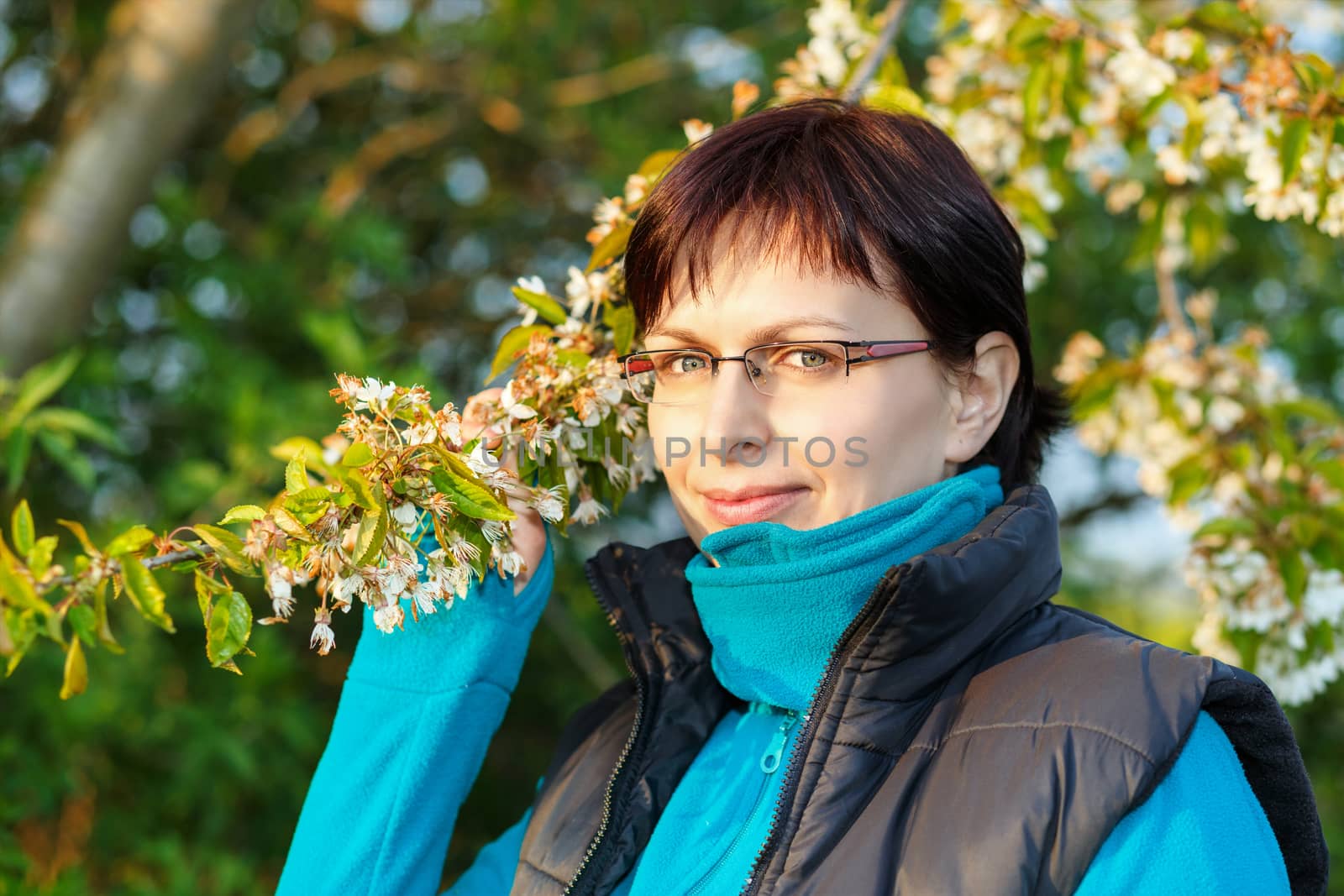 happy smiling middle age woman without makeup outdoor with flowering cherry tree in evening sun