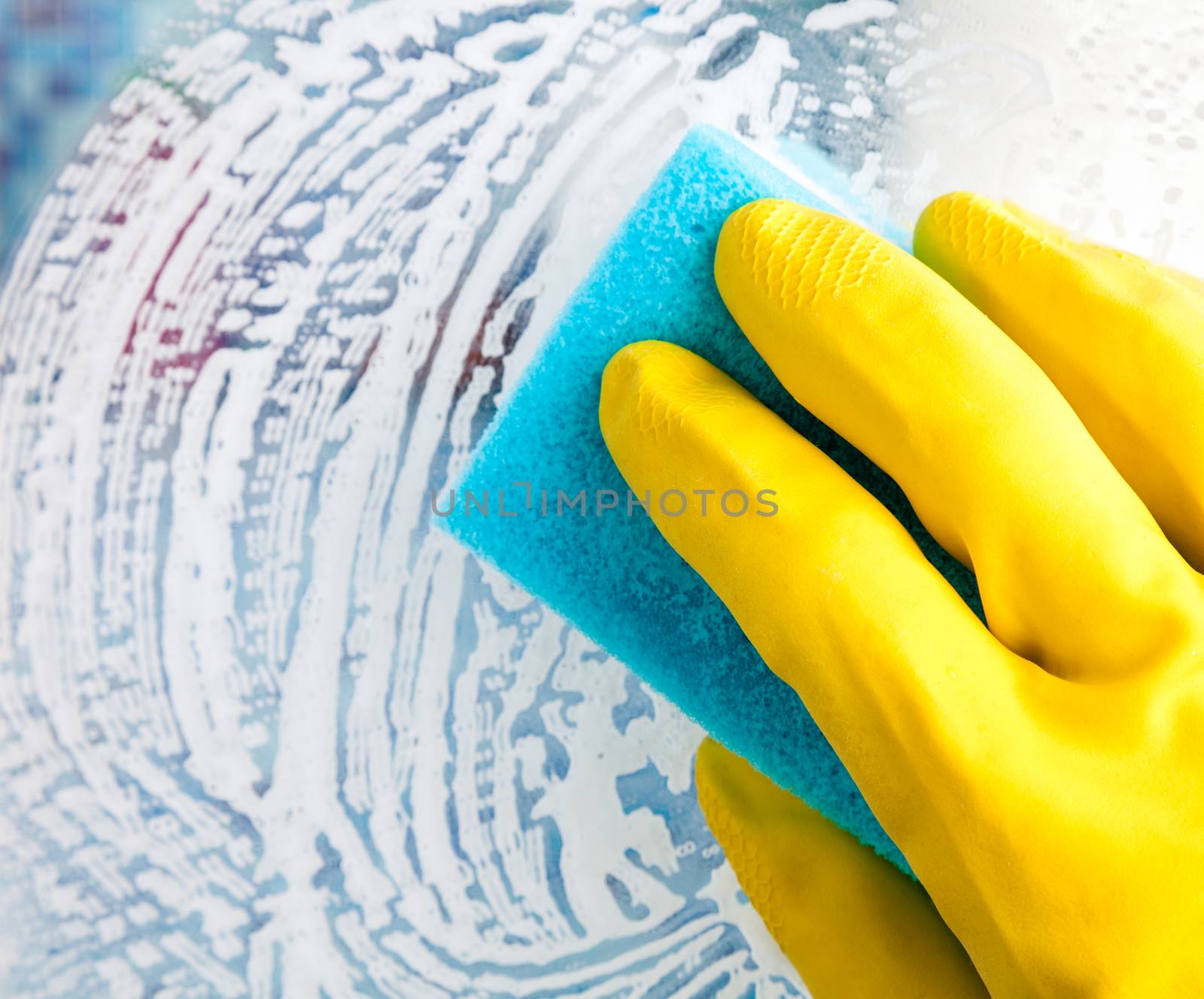 Hand in yellow protective glove cleaning glass with sponge