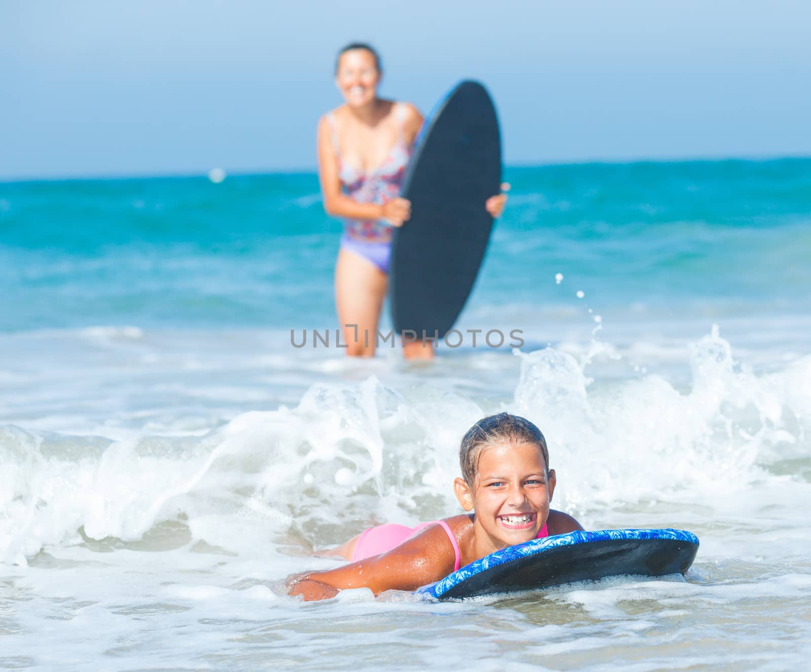 Summer vacation - Happy cute girl and her mother having fun with surfboard in the ocean